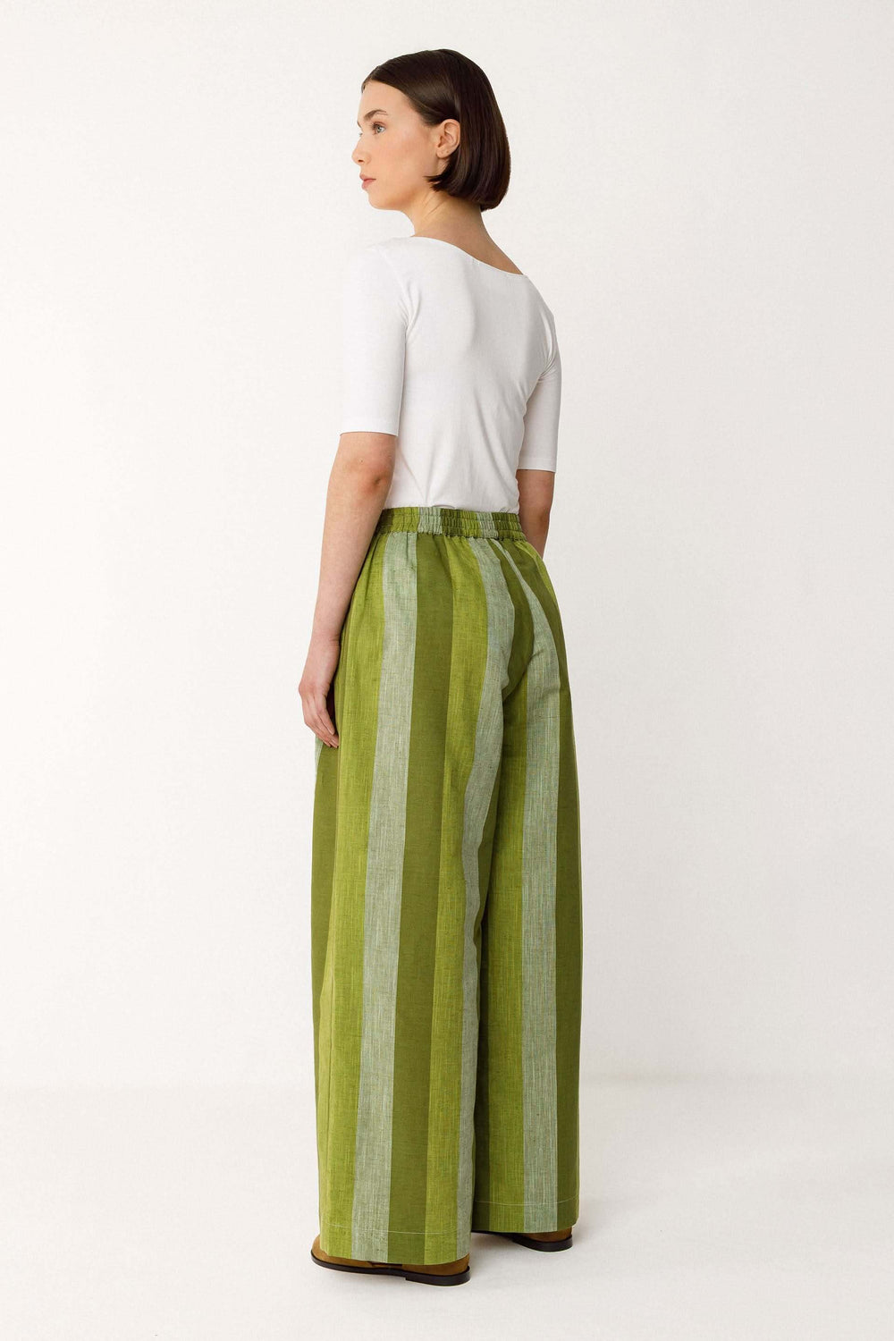 Femme portant un Pantalon Lur large fluide rayé taille haute vert avec poches, offrant une silhouette élégante et allongée.
