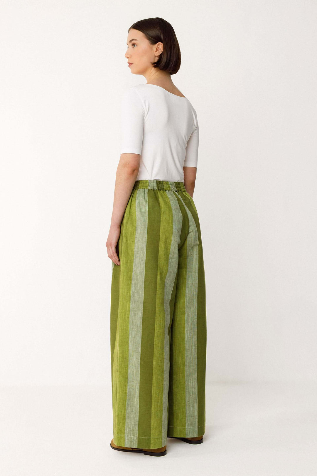 Femme portant un Pantalon Lur large fluide rayé taille haute vert avec poches, offrant une silhouette élégante et allongée.