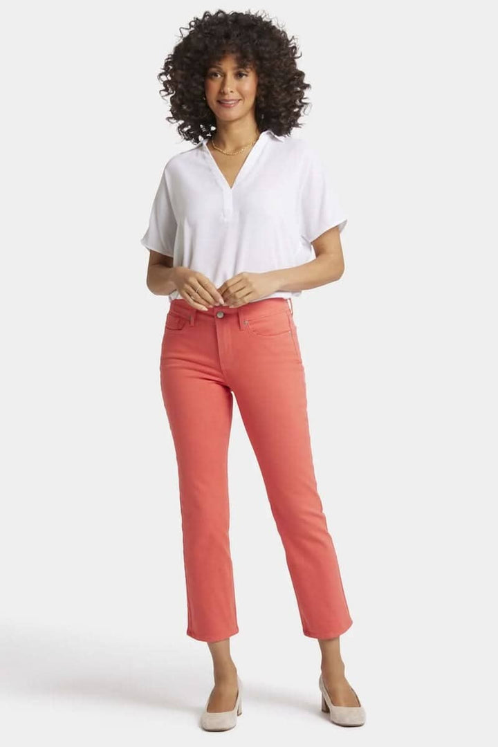 Femme portant un pantalon classique Marilyn rose, coupe droite, avec un haut blanc et des chaussures à talons dans un style décontracté.