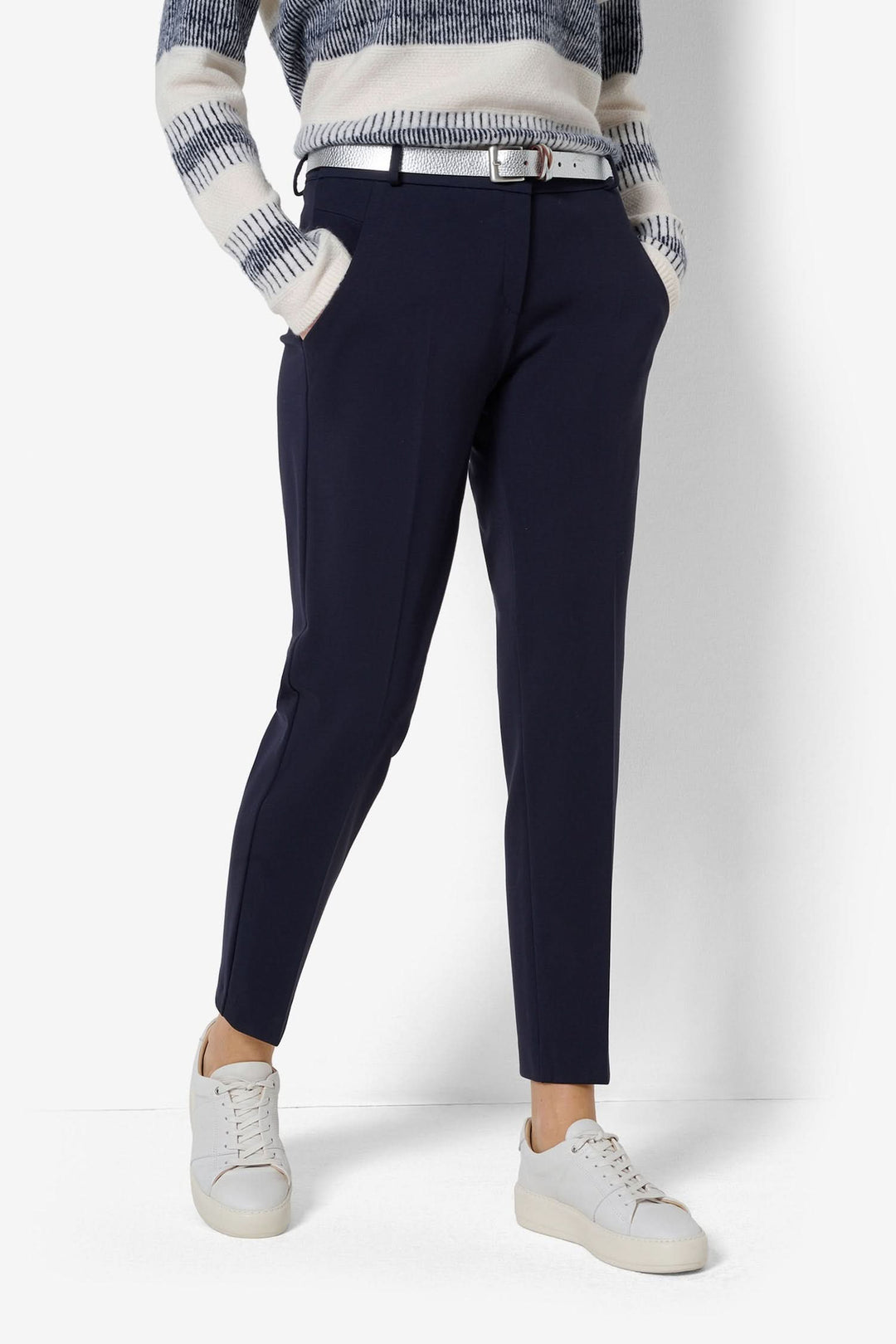 Pantalon chino femme bleu marine avec ceinture, porté avec un pull à rayures et des sneakers blanches.