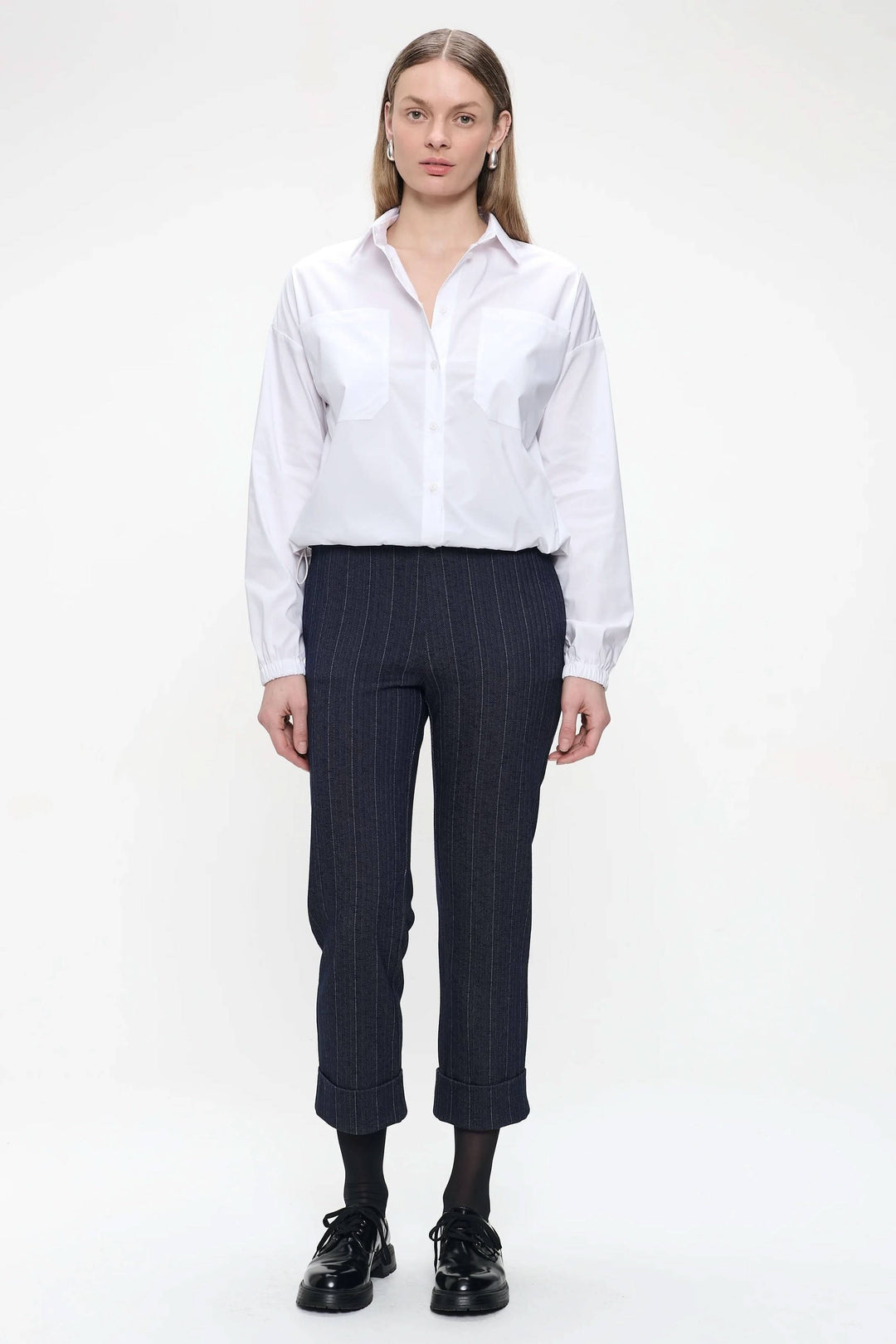 Modèle portant un pantalon à pinces à rayures verticales avec une chemise blanche classique, style moderne et élégant.