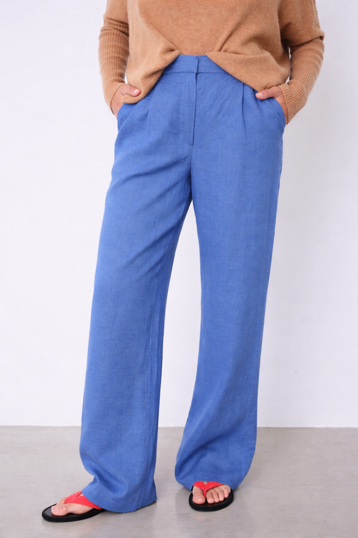 Pantalon Paula large fluide taille haute bleu avec poches latérales, offrant une silhouette élégante et confort maximal.