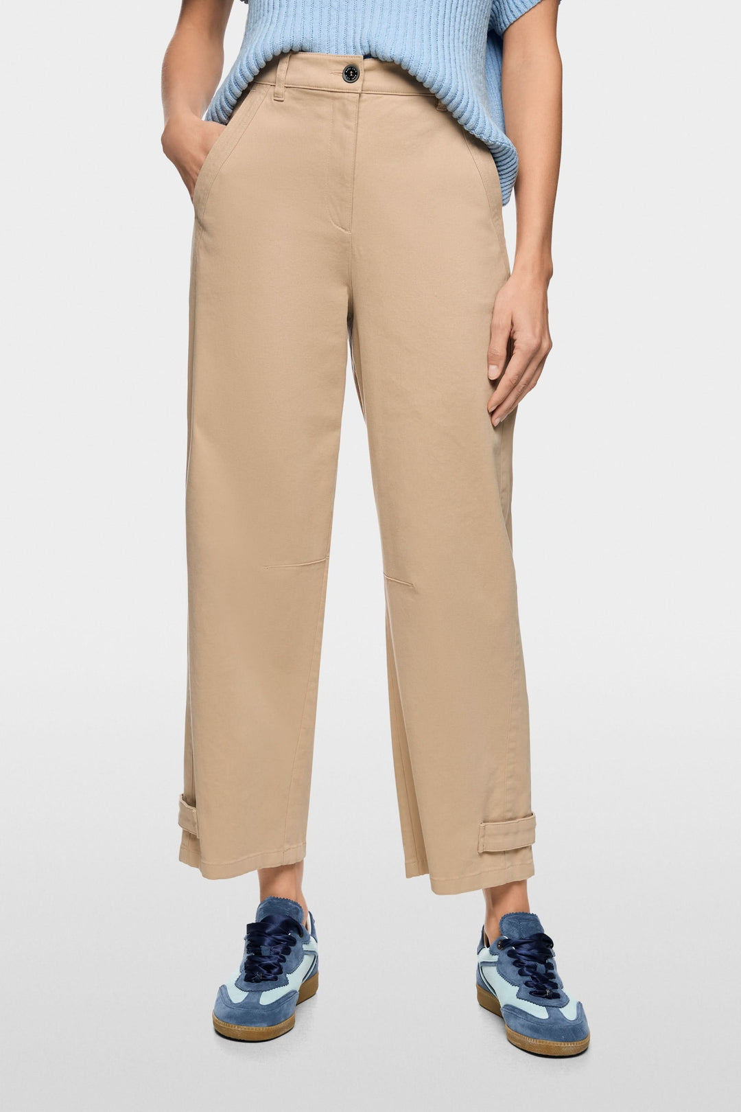 Pantalon RUMA en mélange de coton doux, coupe droite avec taille haute et longueur cheville, couleur beige, porté avec un pull bleu et des sneakers bleus.