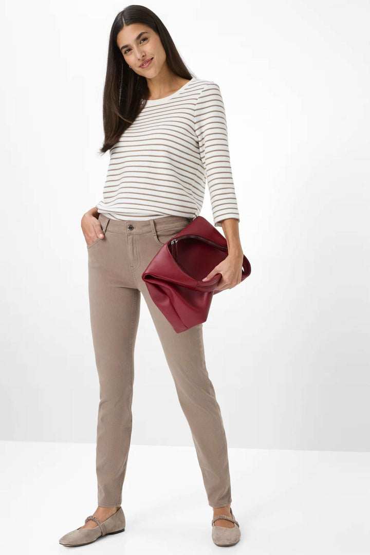 Femme portant le Pantalon Shakira beige avec taille mi-haute et coupe ajustée, associé à un chandail rayé et un sac rouge.