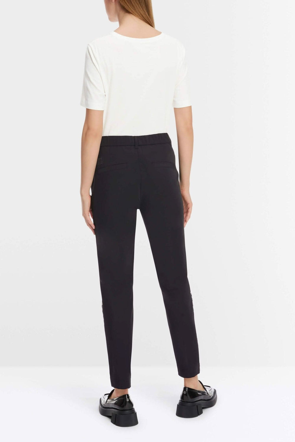 Jeune femme vue de dos portant un pantalon SLIVEN ajusté et une blouse blanche, chaussures noires.