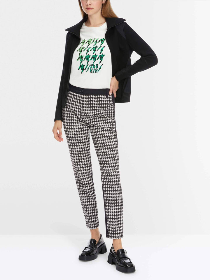 Femme portant le pantalon SLIVEN pied-de-coq avec un t-shirt blanc et une veste noire.