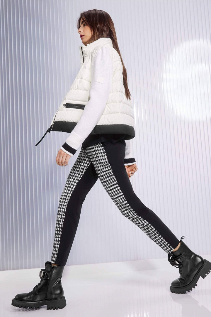 Femme marchant avec un gilet blanc et un pantalon pied-de-coq, style moderne et confortable.