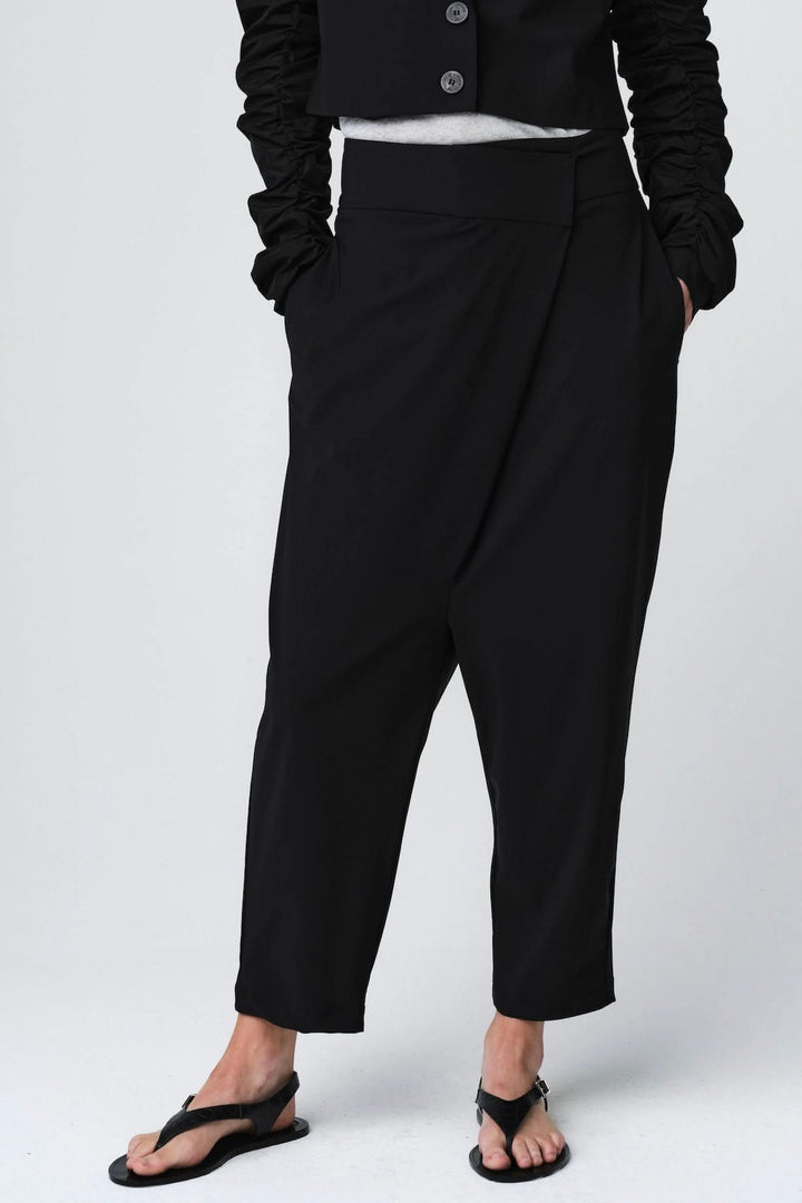 Pantalon ample à taille structurée noir, coupe fluide avec plis subtils et poches latérales, porté avec style moderne.