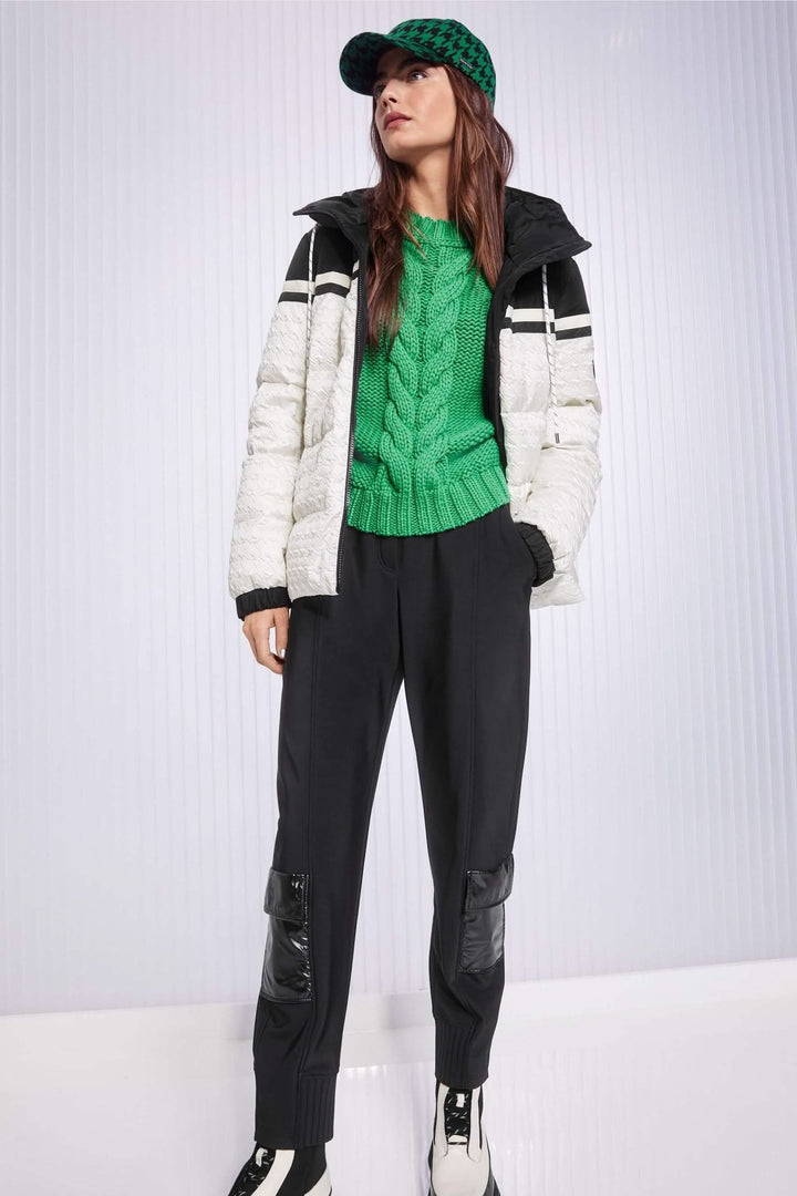 Femme en tenue décontractée avec pantalon noir, pull vert et manteau léger, affichant un style urbain.