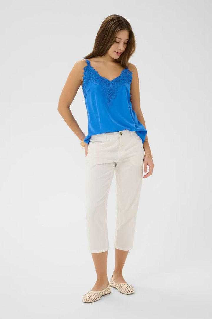Femme portant un pantalon capri Berta coupe droite mi-mollet beige, avec un haut bleu, style décontracté et élégant.