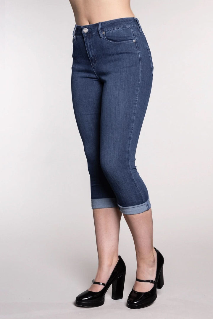 Pantalon capri bleu en denim avec revers, ajusté à la cheville, porté avec des chaussures à talons.