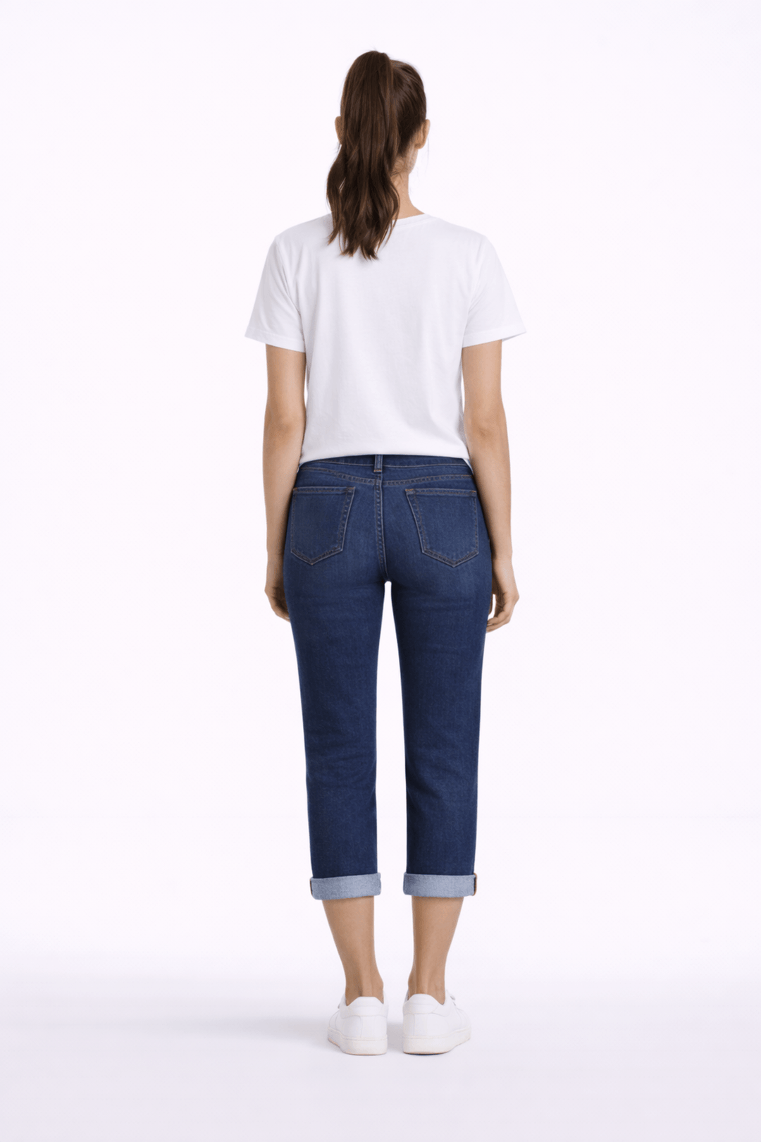Femme portant un pantalon capri ajusté, longueur au mollet avec revers, en denim, vue de dos, associée à un t-shirt blanc.