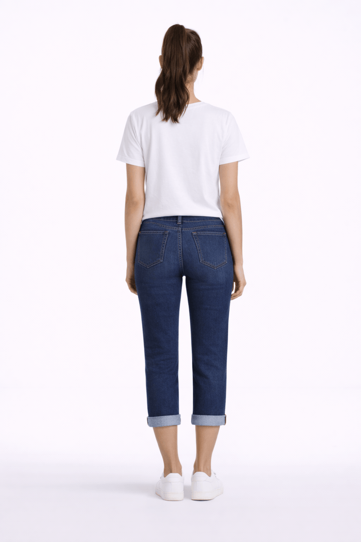 Femme portant un pantalon capri ajusté, longueur au mollet avec revers, en denim, vue de dos, associée à un t-shirt blanc.