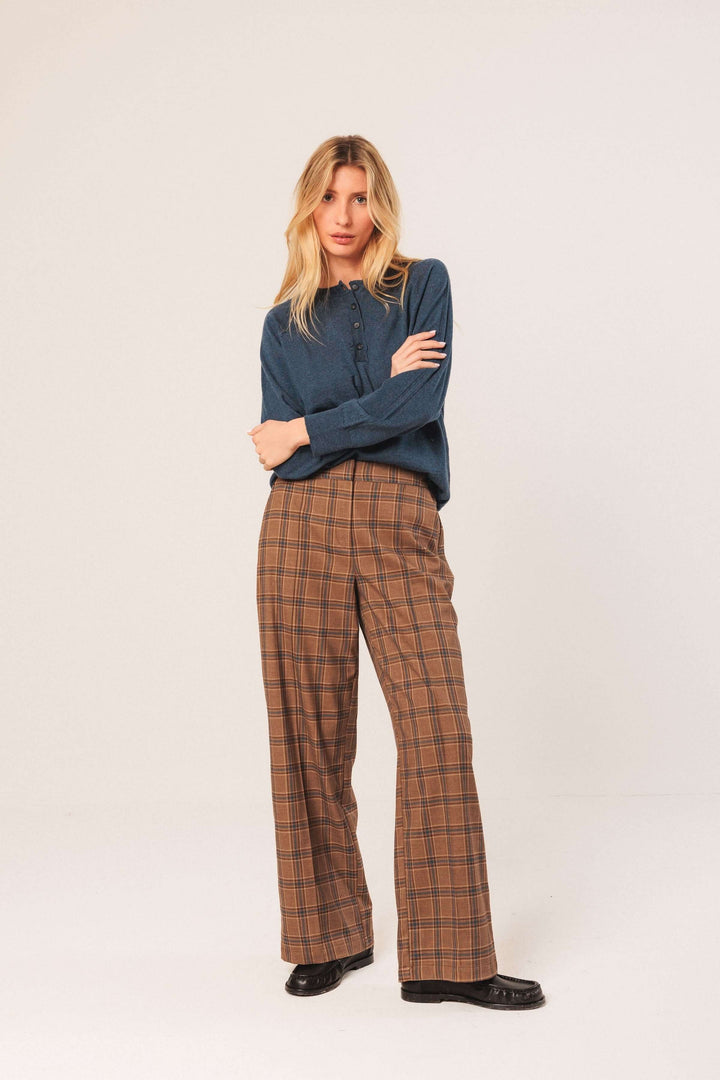Femme portant un pantalon à carreaux large et fluide, associé à un chandail bleu, pose élégante en studio.