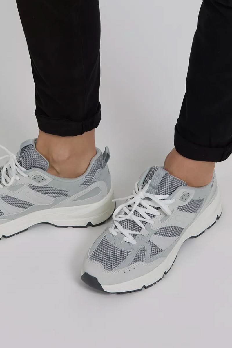 Baskets grises avec semelle blanche, portées avec un pantalon noir, style décontracté.