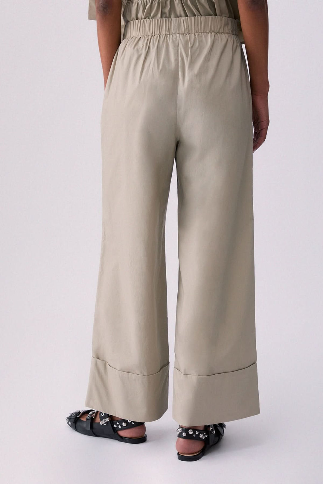 Pantalon chino à jambe large beige avec revers et poches latérales, porté par une personne de dos, décris moi le produit en français.