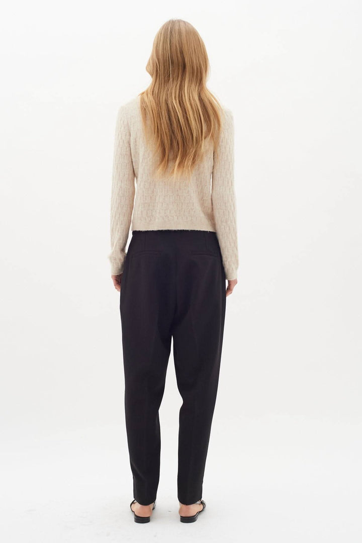 Femme vue de dos portant un pantalon classique noir à plis marqués et un pull beige, look élégant.