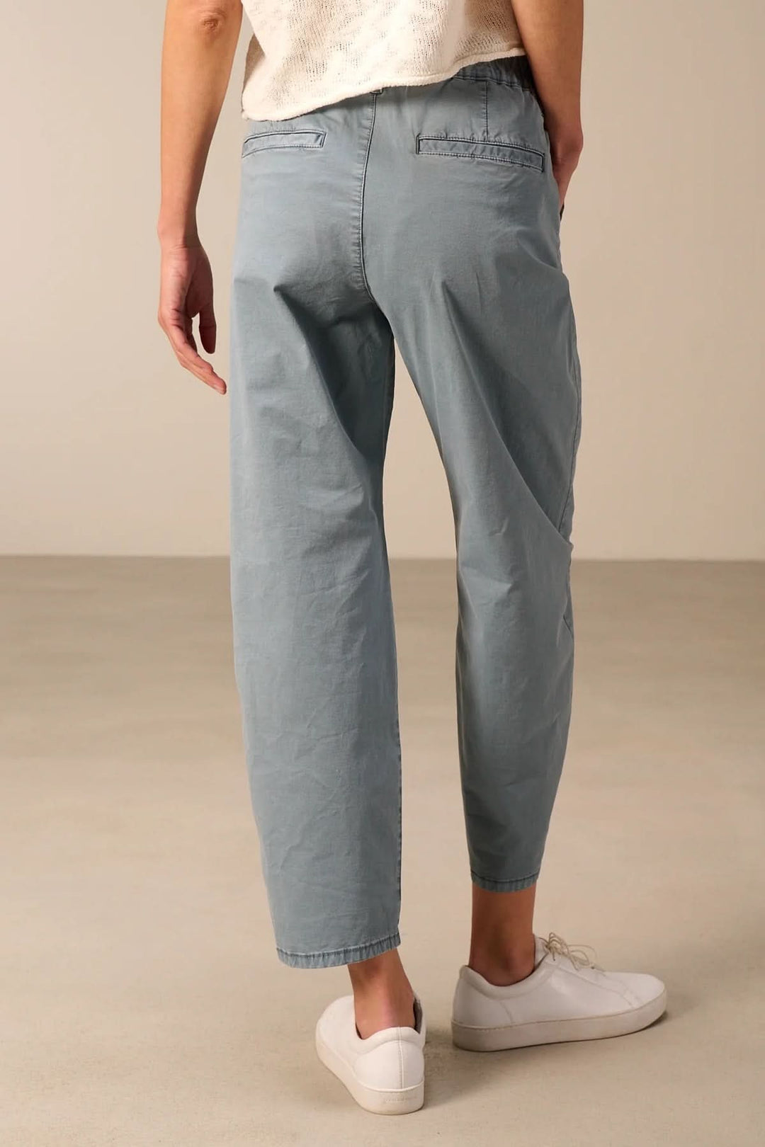Pantalon à coupe décontractée avec taille élastique porté de dos, tissu léger, poches latérales, coupe droite raccourcie, allure moderne.