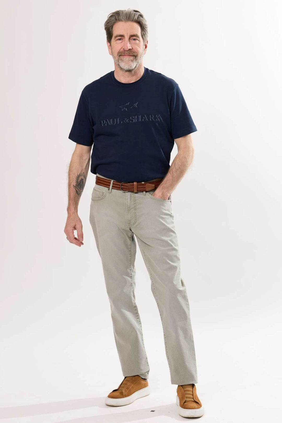 Homme portant un pantalon droit beige et un t-shirt bleu marine, style décontracté avec ceinture en cuir.