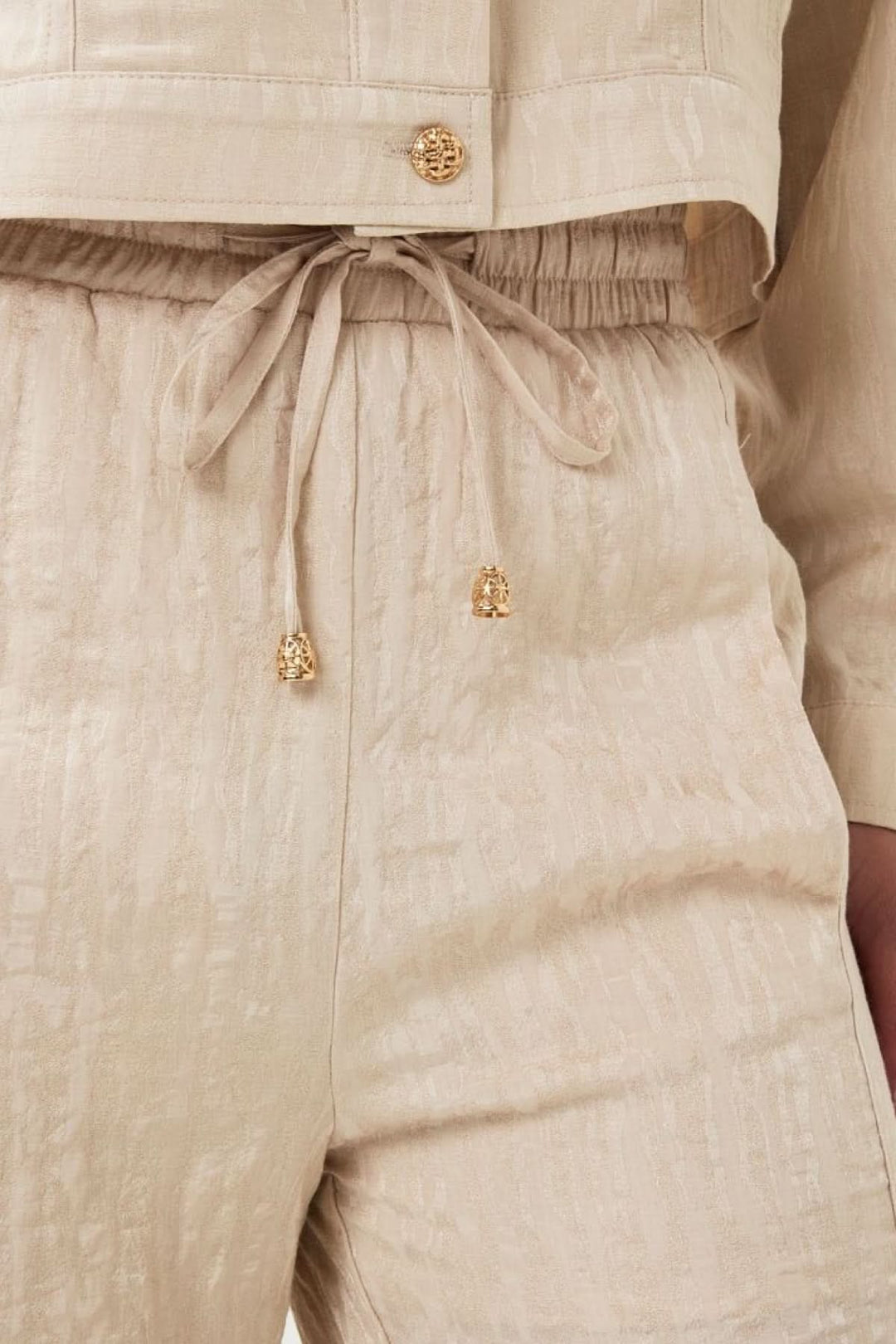 Détail d'un pantalon ample en jacquard texturé beige avec taille élastique et cordon ajustable.