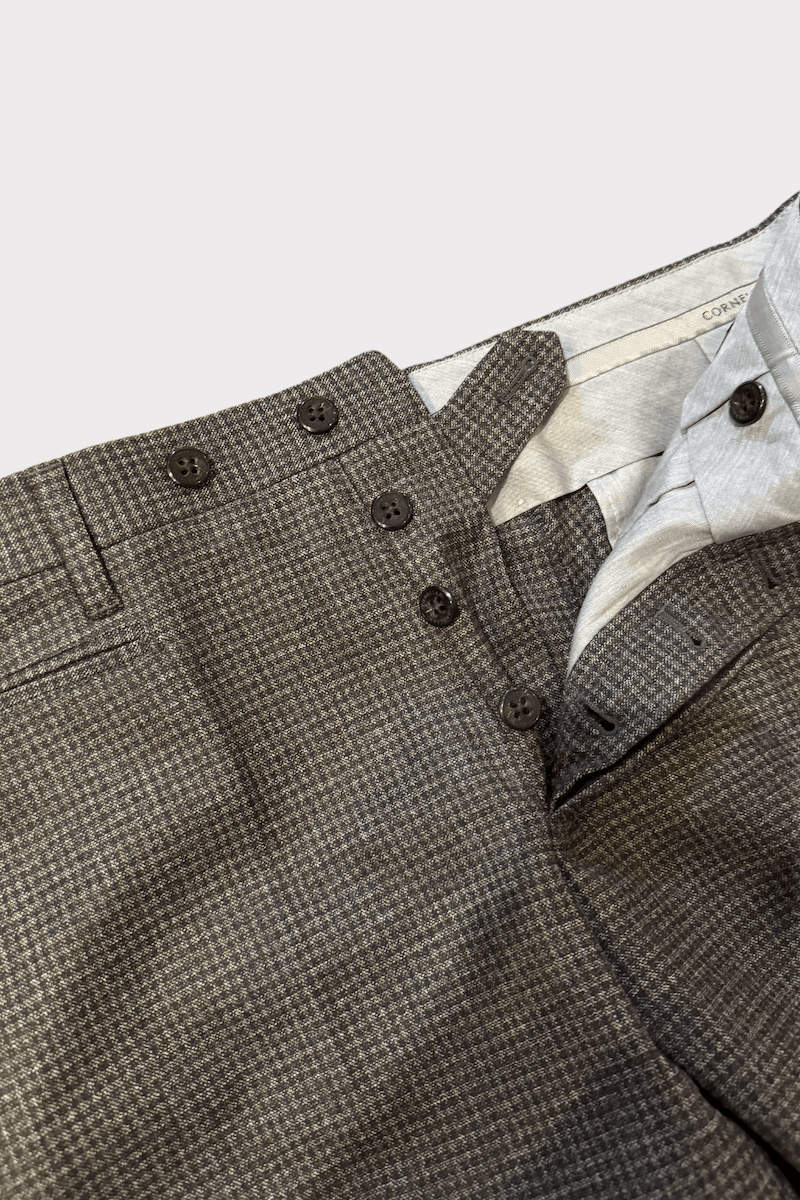 Pantalon en laine à carreaux gris avec boutons dissimulés et poches latérales zippées.