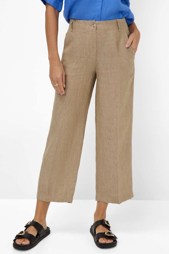 Pantalon en lin MAINE S à jambe large et taille mi-haute, couleur beige, porté avec une chemise bleue et sandales noires.