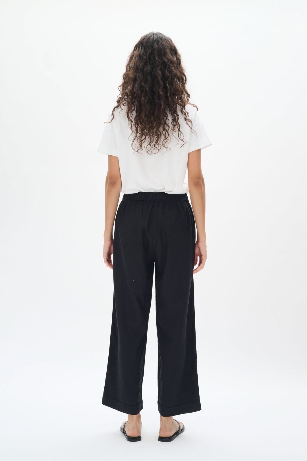 Femme vue de dos portant un pantalon en lin noir à taille élastique et jambes larges.