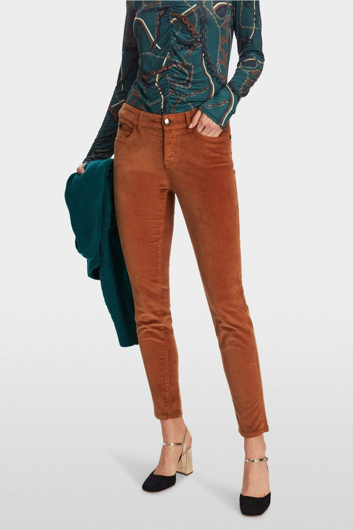 Pantalon en velours orange slim avec jambe raccourcie, porté avec un top à motifs et un gilet.
