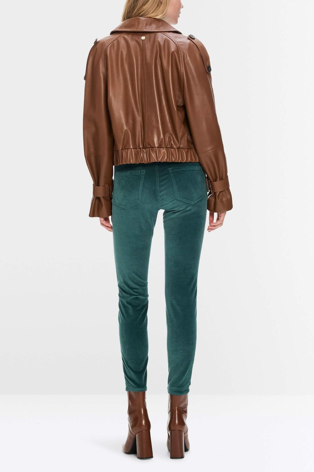 Femme vue de dos portant un pantalon en velours vert et une veste en cuir marron.