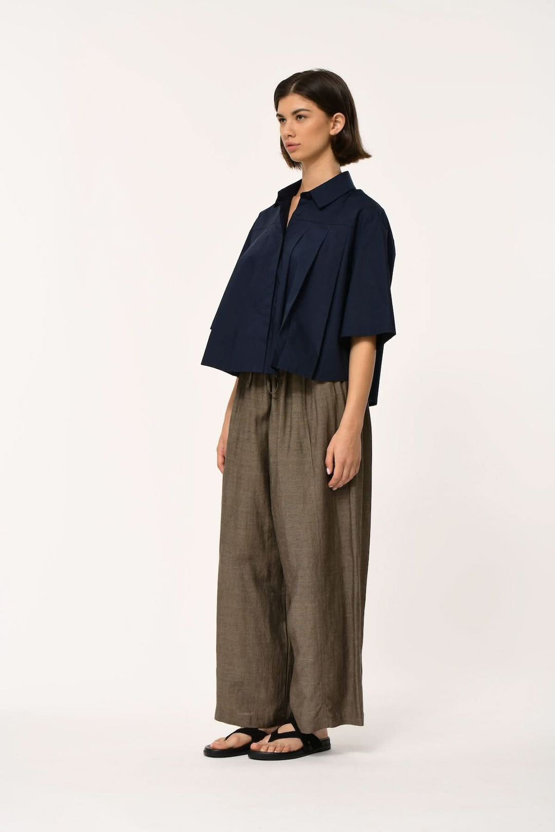 Modèle portant un Pantalon fluide à coupe large JOAN avec chemise bleue et sandales noires, affichant une tenue décontractée élégante.