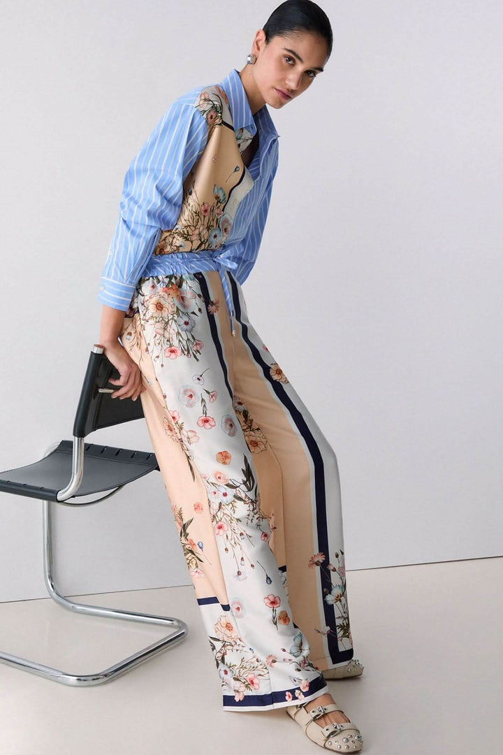 Femme portant un pantalon fluide à motifs et rayures contrastées, tissu léger, coupe ample et élégante, avec chemise assortie.