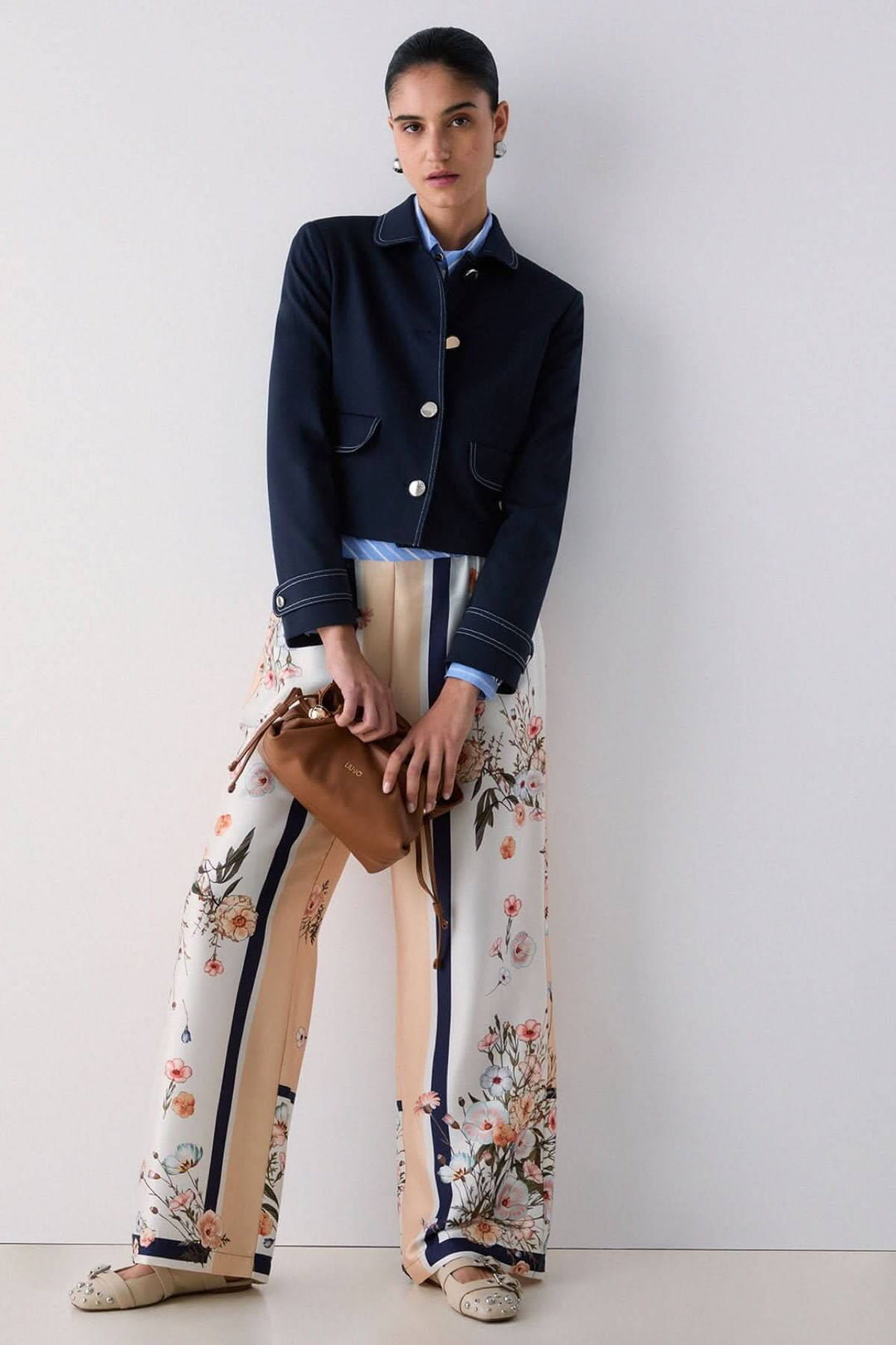 Femme portant un pantalon fluide à motifs et rayures contrastées avec veste noire, exprimant une allure moderne et élégante.
