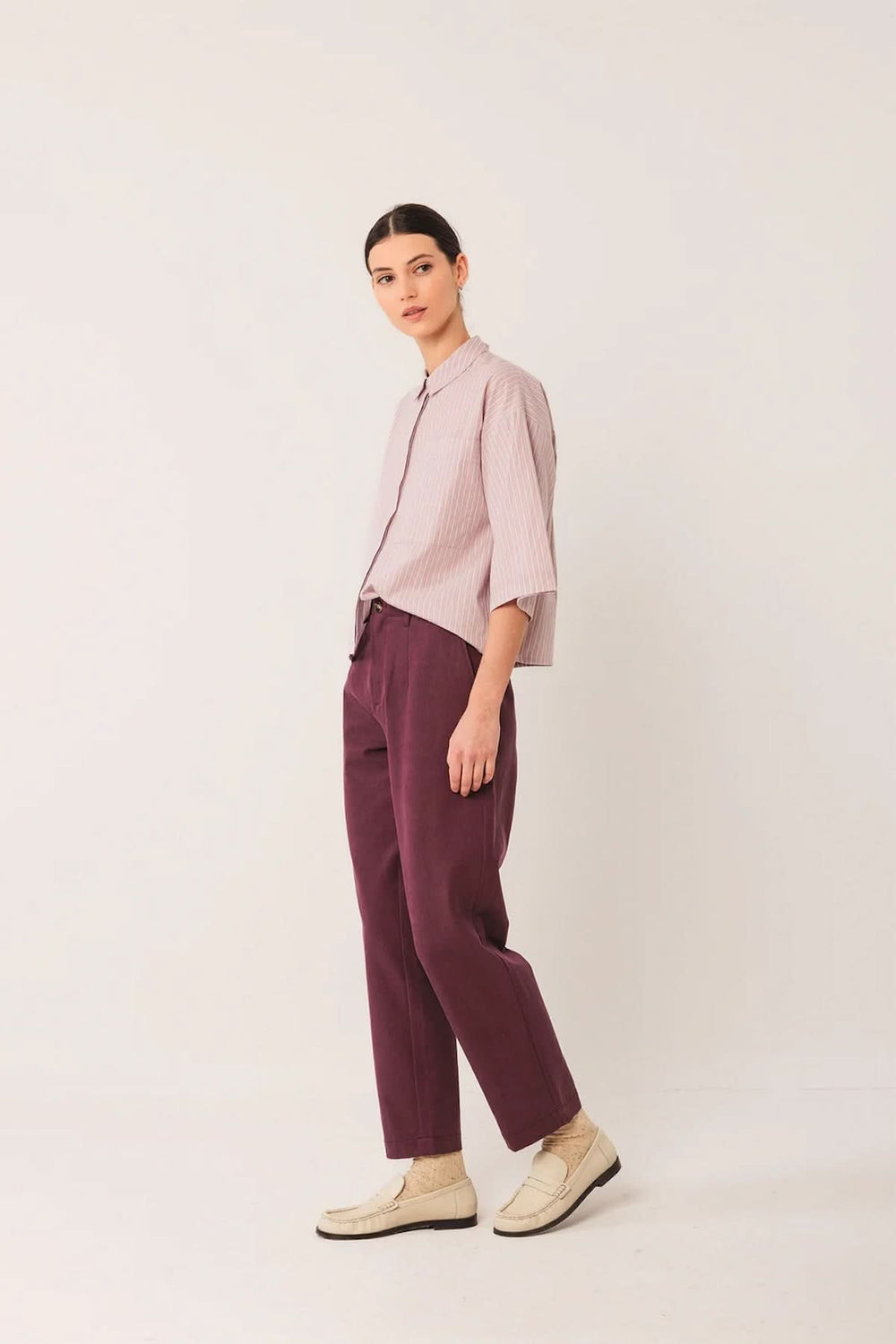 Modèle portant un pantalon à la coupe droite avec taille mi-haute, couleur prune, associé à une chemise oversize et des mocassins beiges.