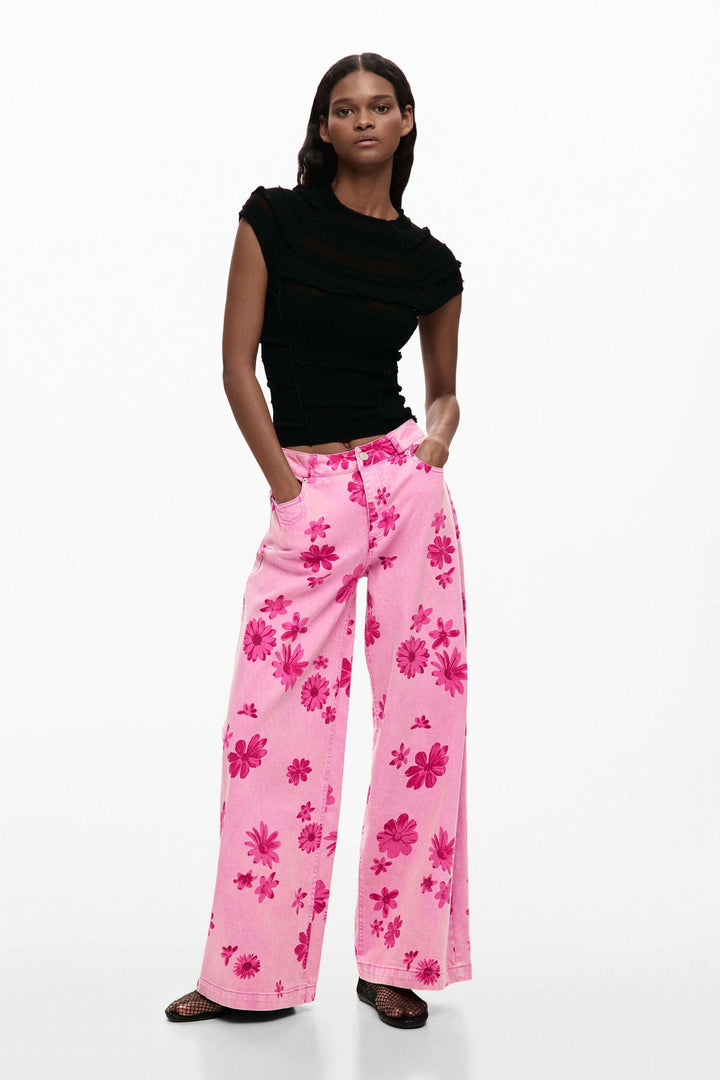 Femme portant un pantalon large à imprimé floral rose avec un haut noir, mode audacieuse et féminine.