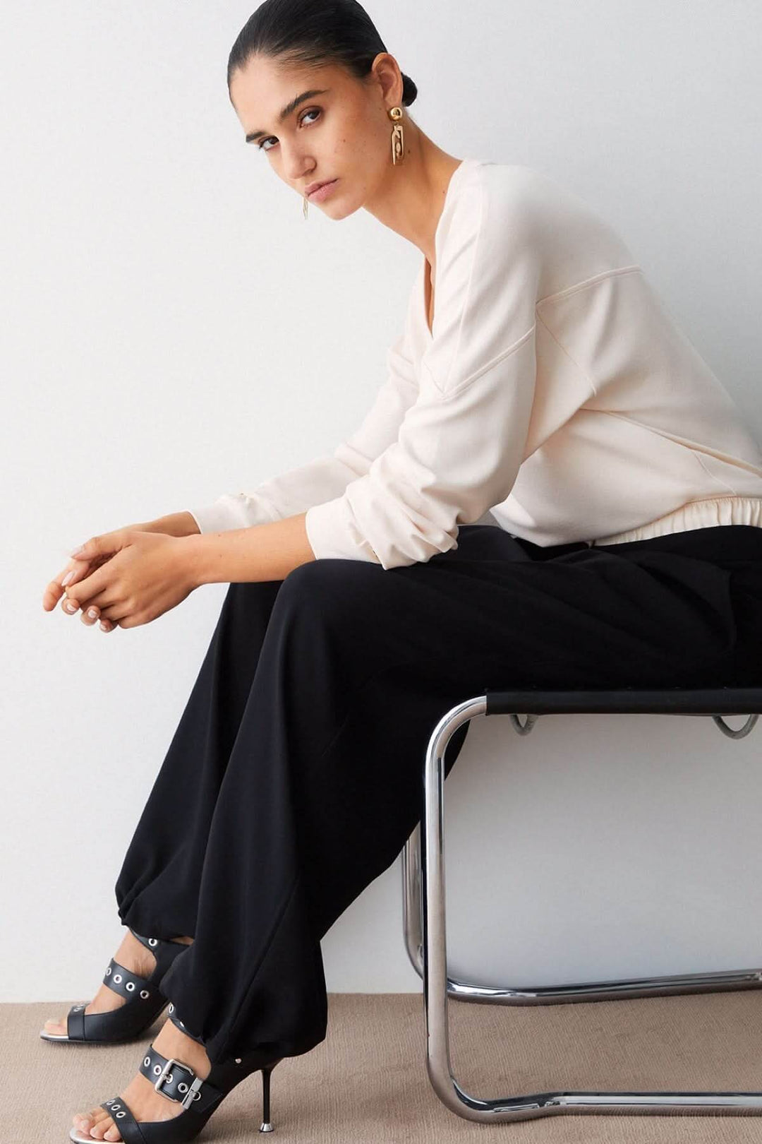 Femme portant un pantalon large à plis avec taille contrastante, assise sur une chaise, en tenue décontractée élégante.