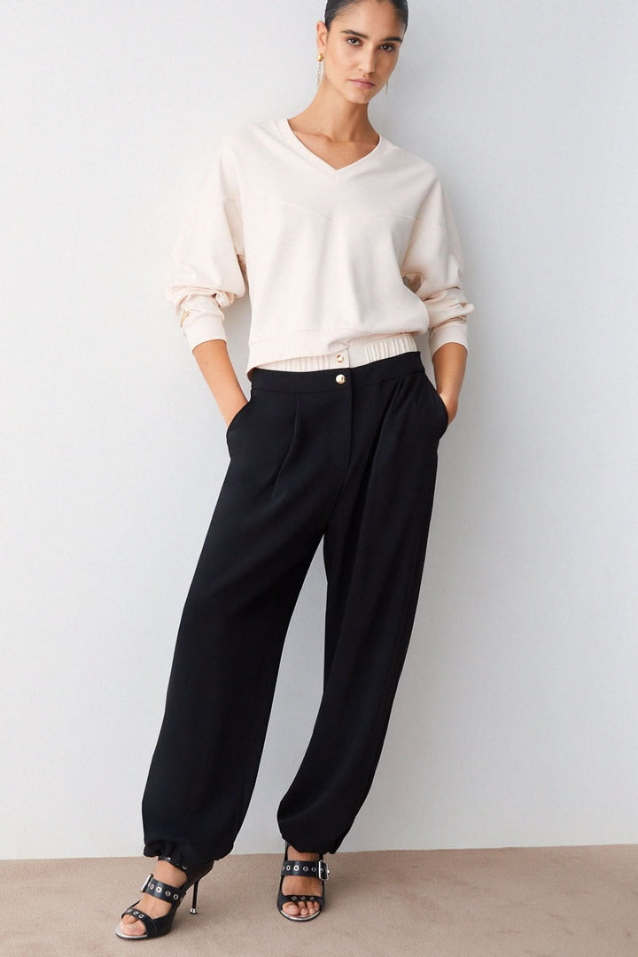 Femme portant un pantalon large à plis avec taille contrastante, boutons décoratifs et coupe fluide élégante.