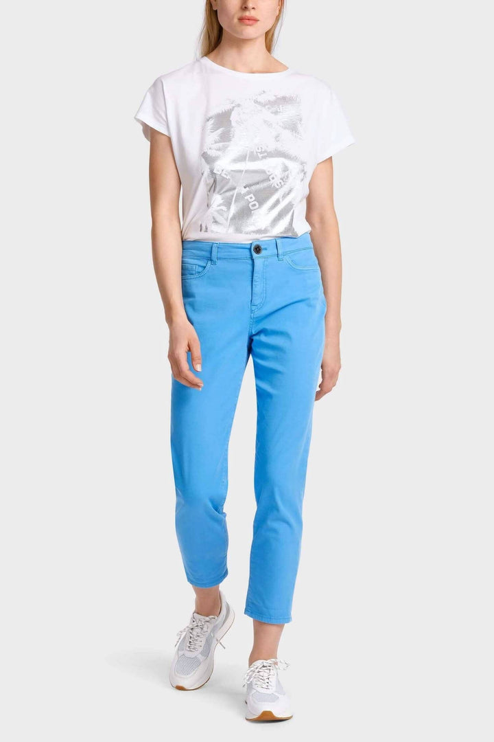 Femme portant un pantalon décontracté bleu et un t-shirt blanc sur fond neutre.