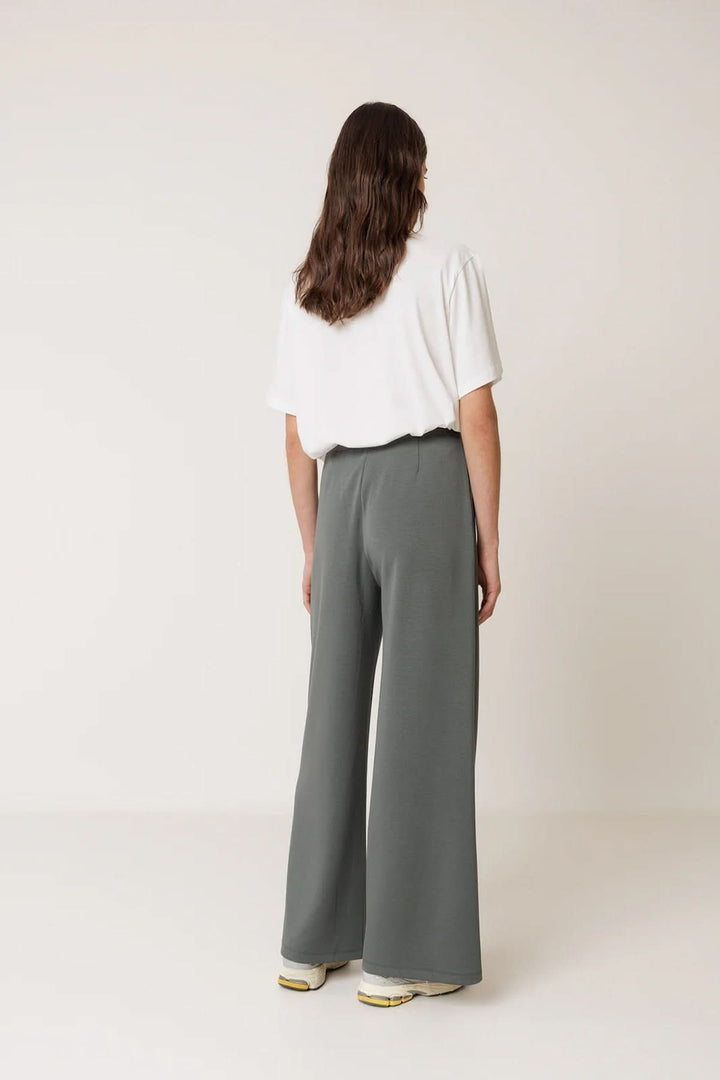 Vue arrière du Pantalon tailleur fluide à plis marqués en gris, porté avec un t-shirt blanc, illustrant une coupe droite et ample.