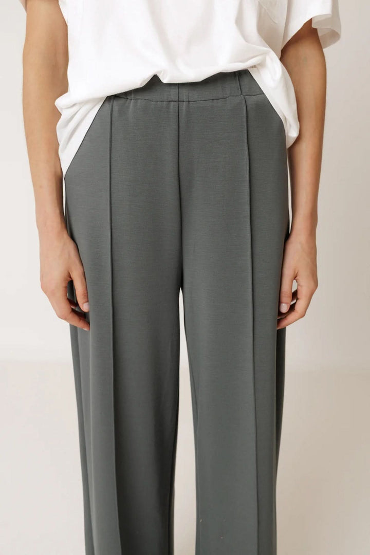 Pantalon tailleur fluide à plis marqués, élégant et moderne avec coupe droite pour allonger la silhouette, en tissu fluide gris.