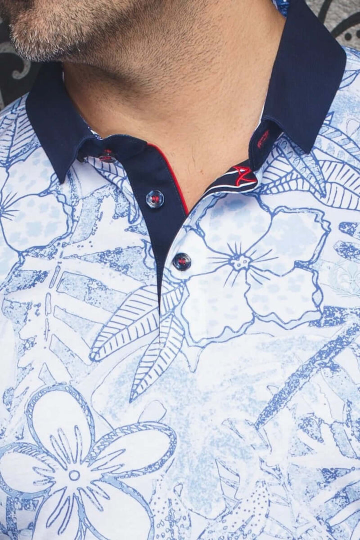 Homme portant une polo élégante avec col contrastant et motifs floraux bleus et blancs.