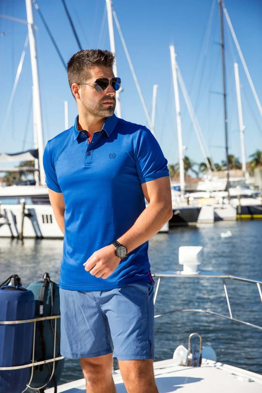 Homme au port portant un polo bleu Eagle, accessoires élégants, ambiance décontractée et sportive.