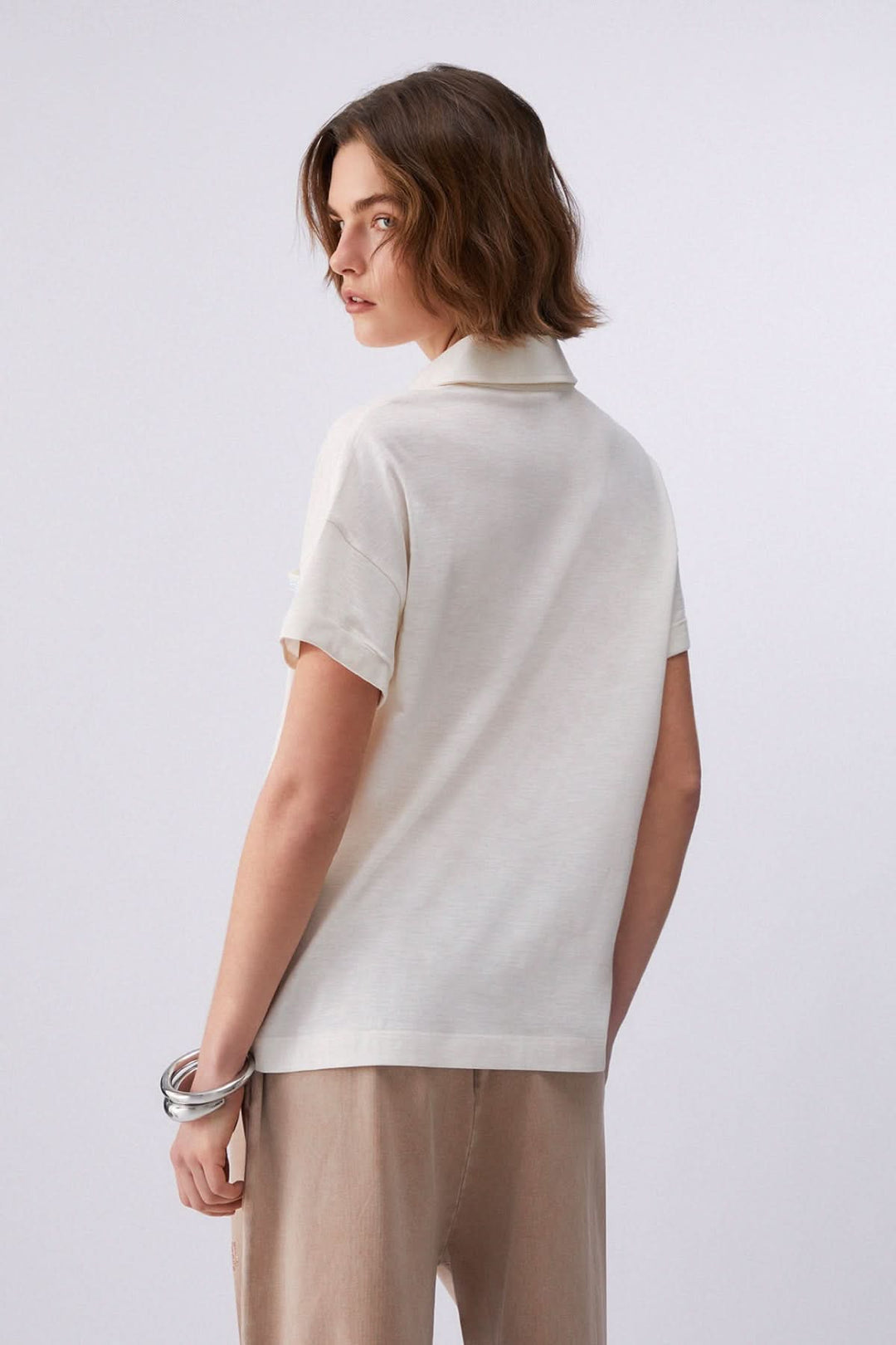 Femme portant un polo à manches courtes avec poche décorative vu de dos, mettant en valeur sa coupe décontractée.