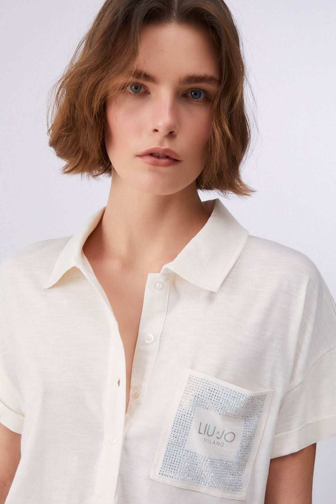 Femme portant un polo à manches courtes avec poche décorative, coupe décontractée et contemporaine, tissu doux et confortable.