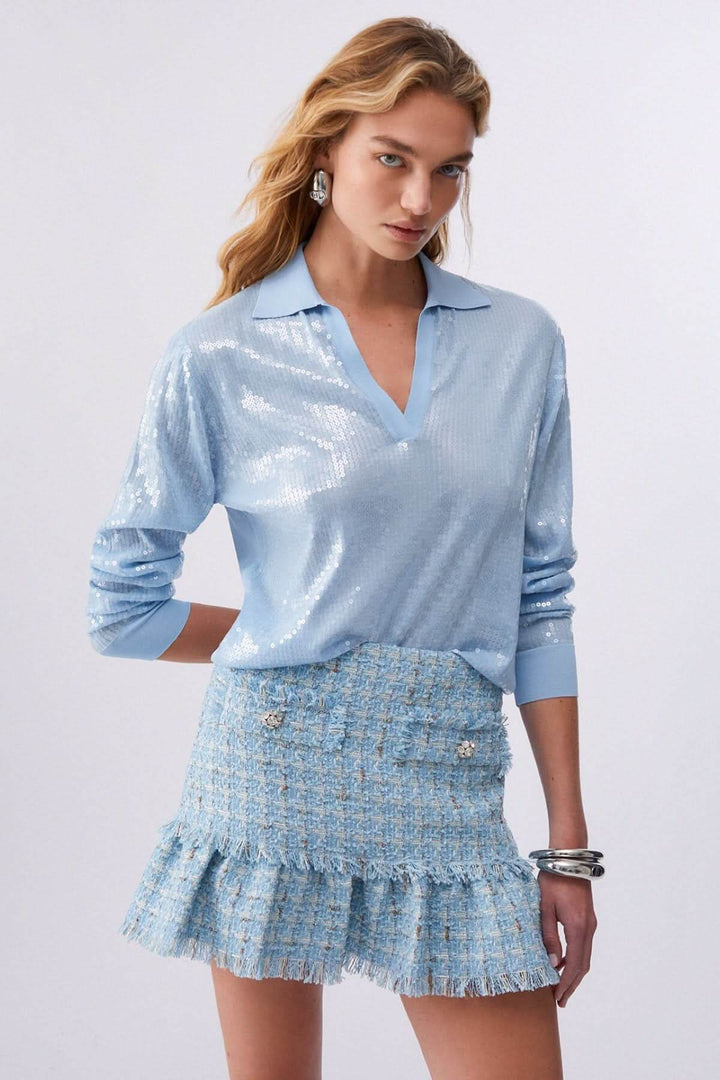 Femme portant un Polo à manches longues avec paillettes bleu, col ouvert et manches longues, conjuguant élégance et confort.