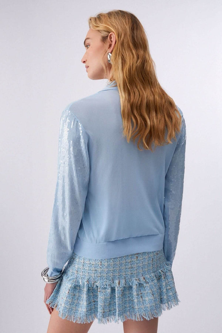 Femme portant un Polo à manches longues avec paillettes, vue de dos, montrant des manches décoratives en maille scintillante.