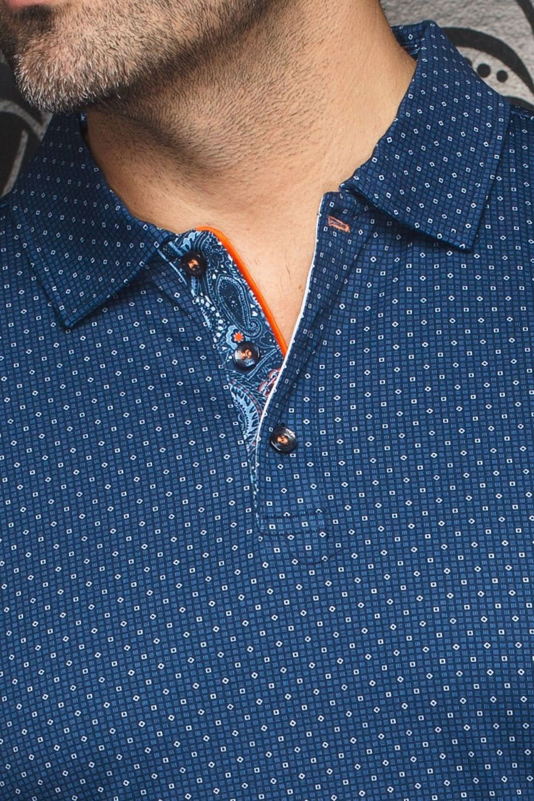 Détail du col et des boutons d'un polo à motif discret, tissu bleu avec finitions contrastantes.