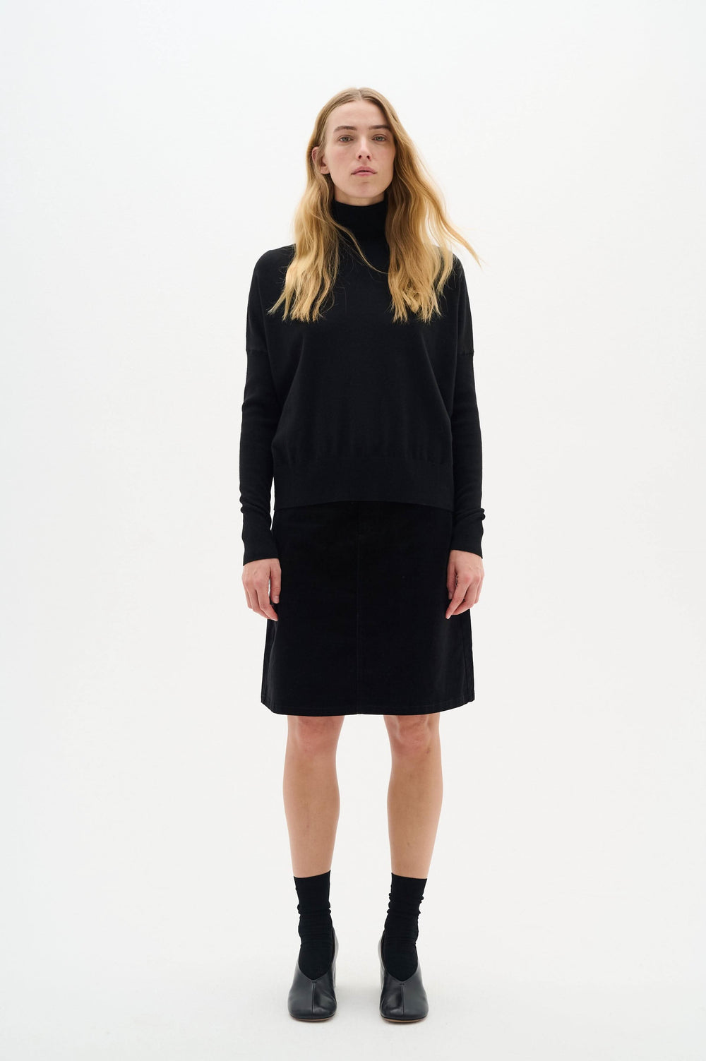 Pull noir à col roulé Kellsie porté avec une jupe, présentant une élégance et un confort optimal.