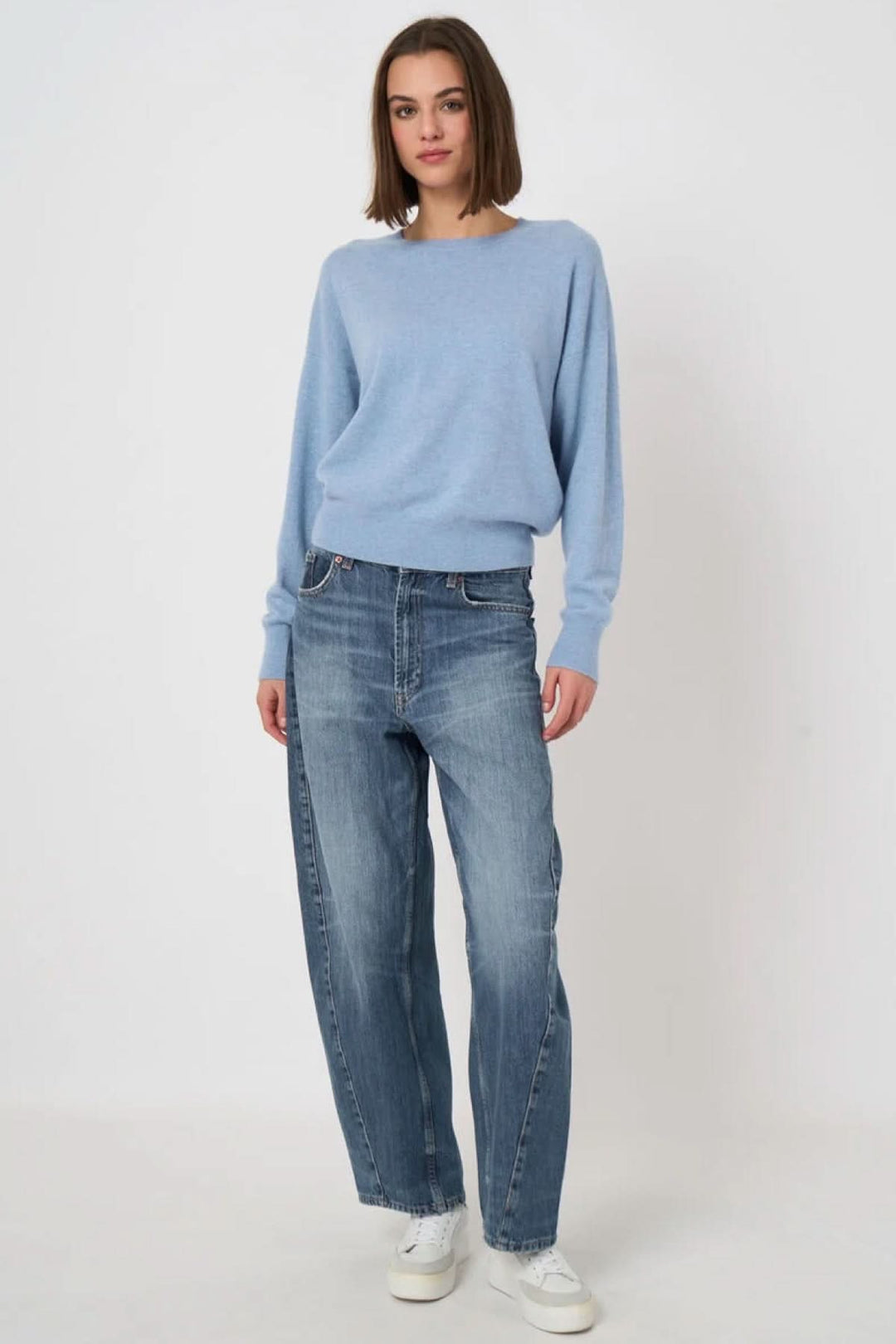 Femme portant un pull à col rond bleu avec jeans, proposant un look décontracté et élégant.