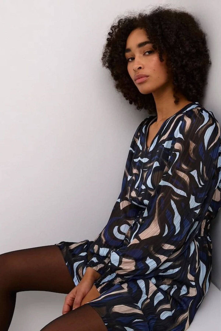 Robe Margo avec motif abstrait en bleu, noir et beige, portée par un modèle assis, manches longues, col en V.