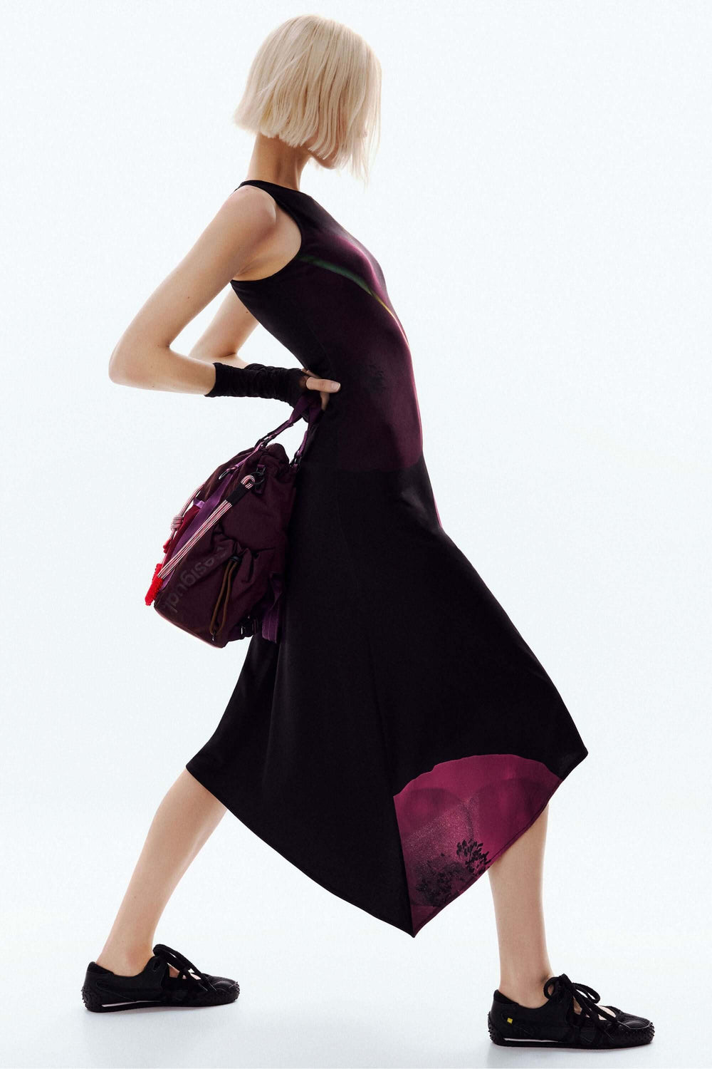 Femme portant une Robe asymétrique coquelicot sans manches avec imprimé floral et silhouette fluide, accessoirisée d'un sac violet.